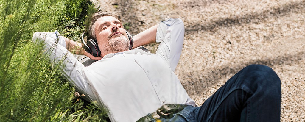 ParkKonto Älterer Mann mit Kopfhörer genießt die Sonne auf einer Parkbank